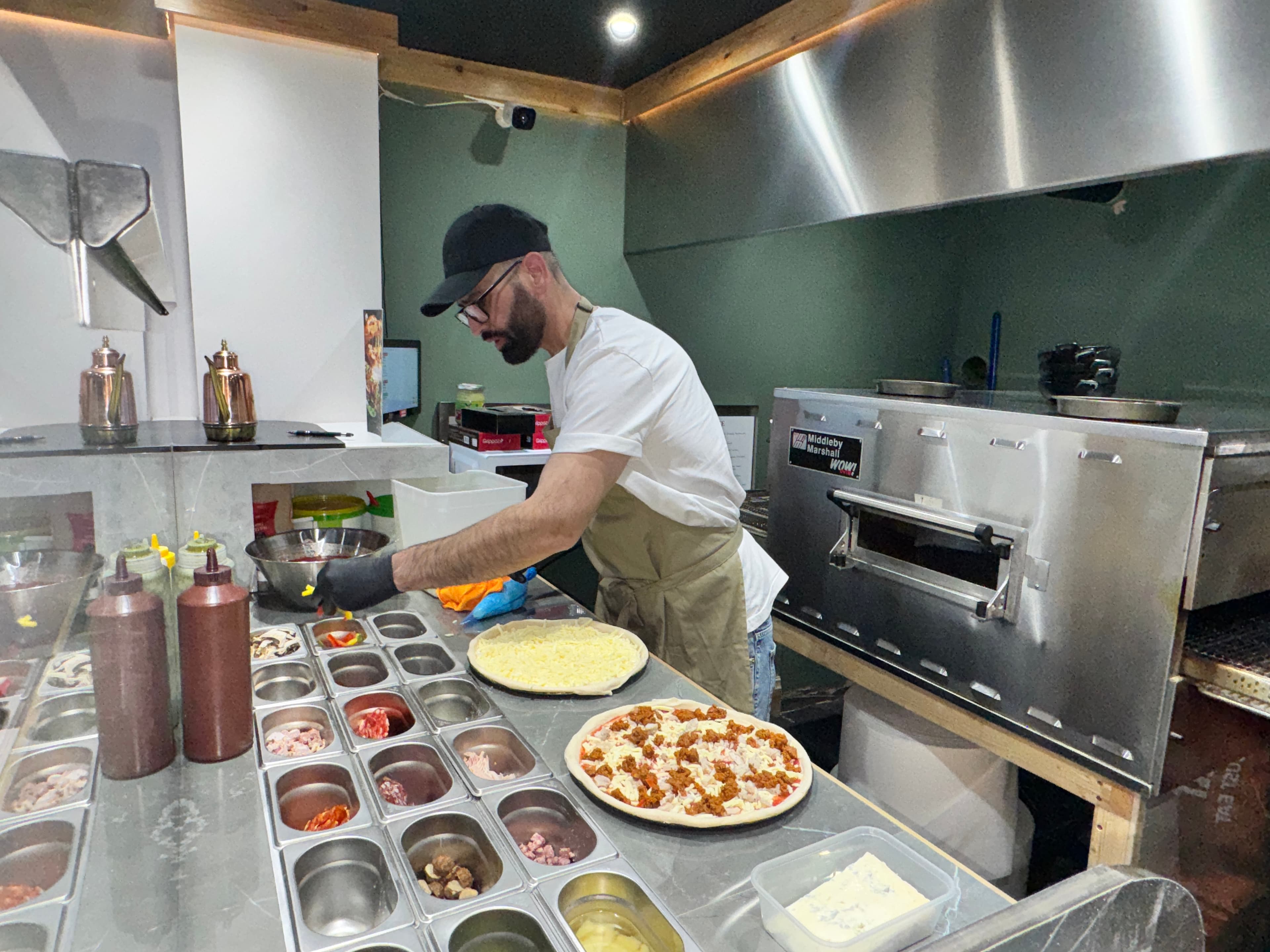 Chef hand-building a pizza at the counter inside 500° Alsager.